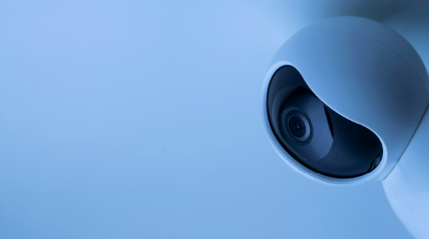 A modern, wall-mounted security camera against a pale blue background, offering a sleek design for discreet monitoring and surveillance.